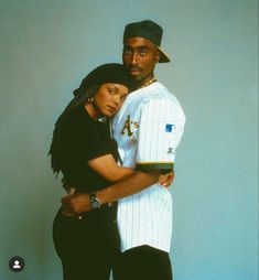 a man and woman standing next to each other in front of a blue wall wearing baseball uniforms