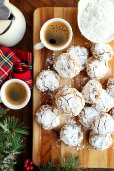 a wooden cutting board topped with powdered sugar covered donuts and two cups of coffee