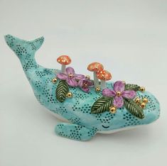 a blue ceramic whale with flowers on its head and two smaller ones in it's mouth