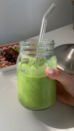 a hand holding a green smoothie in a mason jar with a straw sticking out of it