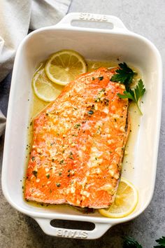 a baked salmon fillet in a white casserole dish with lemons and parsley