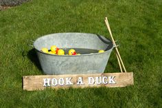 a bucket filled with rubber ducks sitting on top of a green grass covered field next to a sign that says hook a duck