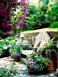 a wooden bench surrounded by potted plants and purple flowers in front of a stone wall