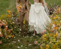 a bride and groom walking through a field with wildflowers in the foreground