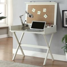 a laptop computer sitting on top of a desk next to a cork board with post it notes