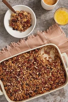 a casserole dish filled with granola next to two bowls of orange juice