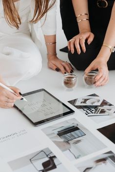 two women sitting at a table with some pictures on the table and one holding a tablet