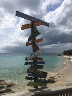 a wooden sign on the beach pointing in different directions