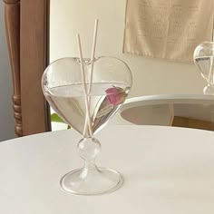 a heart shaped vase with sticks sticking out of it on a white tablecloth covered dining room table