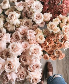 a person standing next to a bunch of flowers on top of a wooden floor in front of a wall