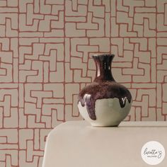 a brown and white vase sitting on top of a table next to a wall paper