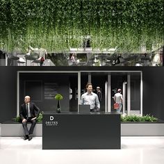 two men in suits are sitting on the outside of a building with greenery hanging from the roof