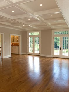 an empty living room with hard wood flooring and white trim on the doors, windows, and french doors