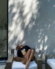 a woman laying on top of a wooden bench next to a dog