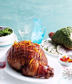 a ham is sitting on a white plate next to some wine glasses and other food