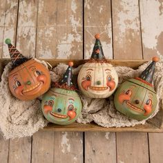 three pumpkins with faces painted on them sitting in a wooden box, one is wearing a party hat and the other has a clown's head