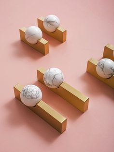 four marble knobs are placed next to each other on a pink surface with gold bars