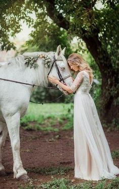 a woman in a white dress standing next to a white horse and holding the bridle