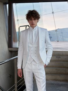 a man in a white tuxedo standing next to some stairs and looking at the camera