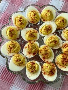 deviled eggs with mustard sprinkled on them in a glass dish sitting on a red and white checkered tablecloth