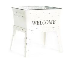 a white welcome sign sitting on top of a wooden table next to a planter