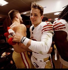 two football players are hugging each other in the locker room with one holding his arm around the other's chest