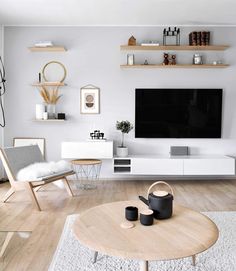 a living room with white walls and wooden furniture, including a flat screen tv on the wall