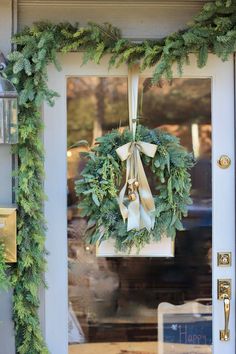 a wreath hanging on the front door of a house decorated with greenery and bells