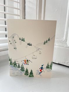 a card with skiers skiing down a snowy mountain slope and pine trees on the side