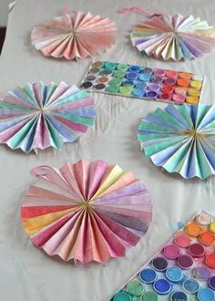 colorful paper fans are arranged on a table with watercolors and crayons