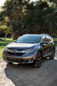 the new honda cr - v is parked on a dirt road in front of some trees