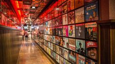 a long hallway with many posters on the wall and people walking down one side in front of them