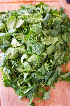 a pile of green leafy vegetables sitting on top of a wooden cutting board