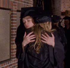 a woman in a graduation gown hugs another woman's shoulder while she is wearing a black cap and gown