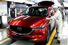 a man standing next to a red car in a garage with other people working on it