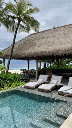 lounge chairs next to a swimming pool with thatched roof and palm trees in the background