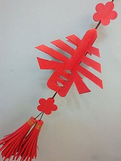 a red paper sign hanging from a string with tassels and flowers on it