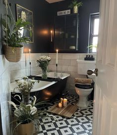 a black and white tiled bathroom with candles on the floor, potted plants in front of the bathtub