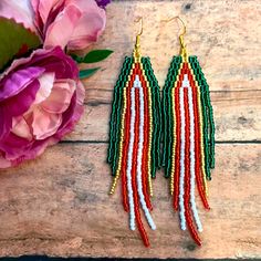 red, white and green seed beaded earrings on wooden table next to pink flowers