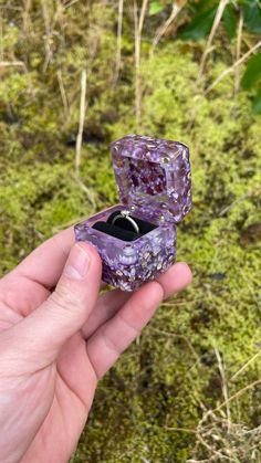 someone is holding an open ring box in their hand with moss growing on the ground