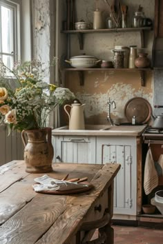 a rustic kitchen with an old wooden table and flowers in a vase on the counter