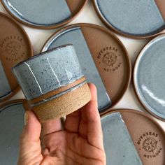 a person holding up a blue and brown cup in front of some coasters on the wall