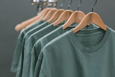 a row of green t - shirts hanging on wooden hangers