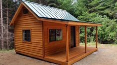 a small wooden cabin in the woods with a metal roof and green shingled windows