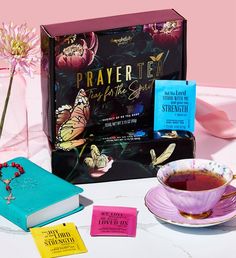 a cup of tea next to a book and some cards on a table with pink flowers