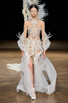 a model walks down the runway in a white dress with feathers on her head and shoulders