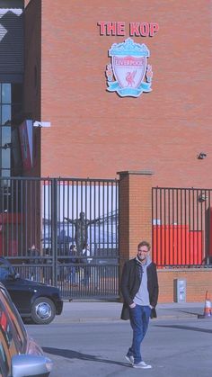 a man walking down the street in front of a building with a sign that says the kop