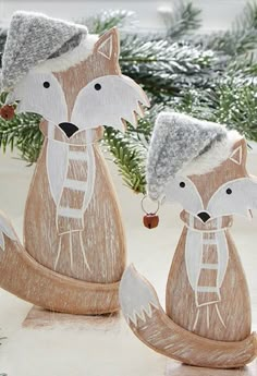 two wooden foxes with hats and scarfs sitting next to each other on snow covered ground