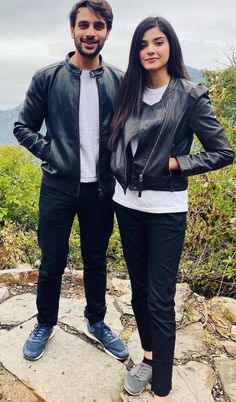 a man and woman standing next to each other on top of a rock covered hillside