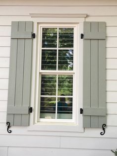 a white house with green shutters and a woman looking out the window from behind